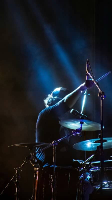Drummer silhouetted in a blue stage beam