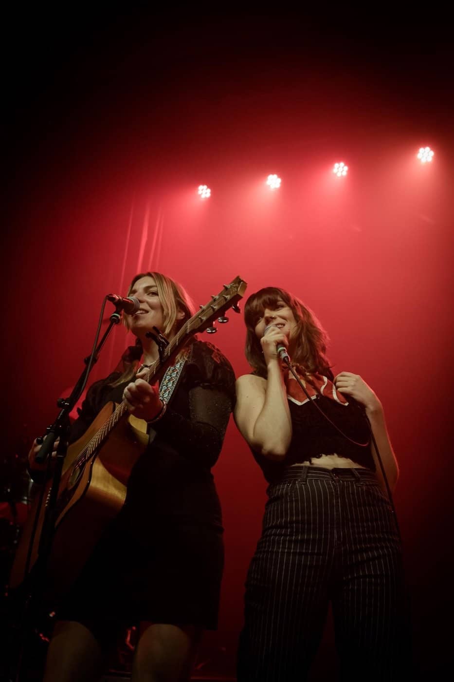 Two singers sharing a mic under red stage lights
